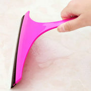 A hand holds a pink car mirror wiper, wiping suds from a light-colored tiled surface.